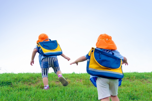 子供が鞄を持って土手をかけあがる様子